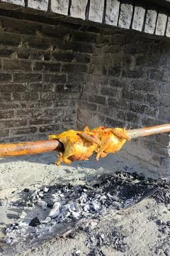 Two chickens roasting on a spit on coals in sunlight Foto stock