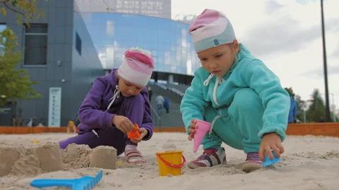 Two children 4-5 years old sitting in sandbox, playing with toys and buckets Video stock 138044103