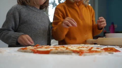 Two children adding ingredients to a homemade pizza Stock Footage 255017718