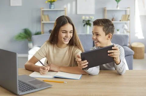Two children are happily doing their homework and having fun using modern Stock Photos