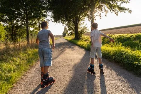 Two children are inline skating along a dirt path framed by trees and field.. Stock Photos