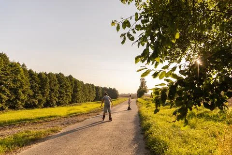 Two children are inline skating along a quiet pathway surrounded by lush gr.. Stock Photos