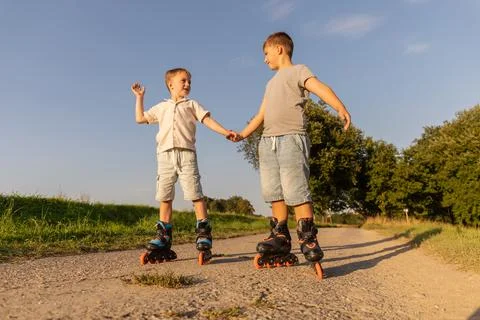 Two children are inline skating happily on a dirt path, enjoying a bright s.. Stock Photos