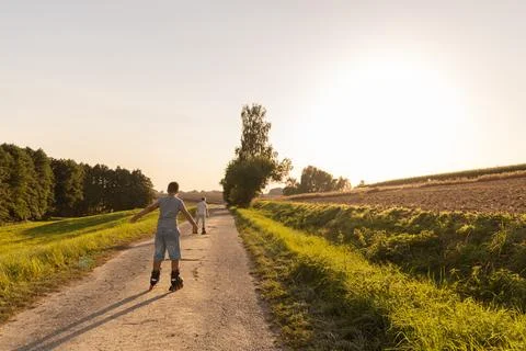 Two children are inline skating along a calm path surrounded by greenery. T.. Stock Photos