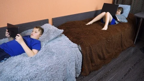 Two children are lying on the bed and playing on the laptop. Stock Footage 99045780