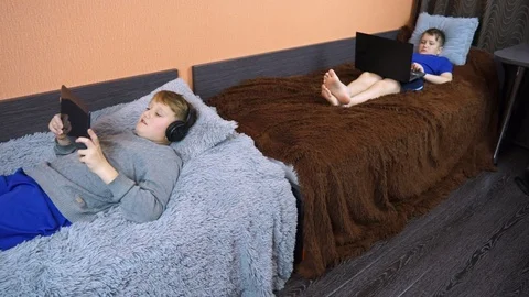 Two children are lying on the bed and playing on the laptop. One does not work t Stock Footage 99045820