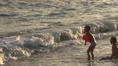 Two Children Are Playing With Big Waves on Sea Beach in Hot Evening in Summer Stock Footage 65262602