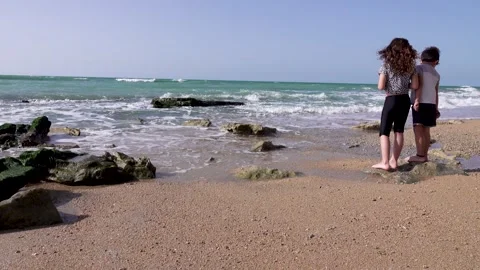 Two children are standing on the beach The water covers the feet 스톡 동영상 208035995