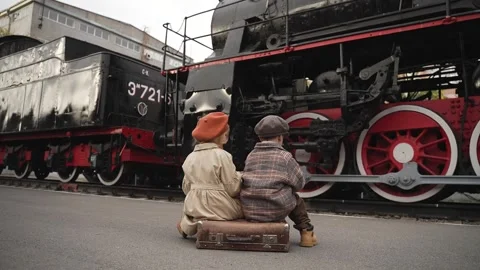 Two children in autumn clothes sit on suitcase on the platform Stock Footage 314761603