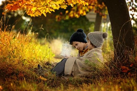 Two children, boys, hugging under blanket, sitting under a tree on a sunny au Stock Photos