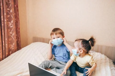 Two children brother and sister in medical masks using laptop Stock Photos