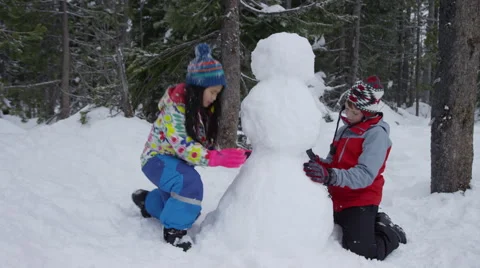Two children building snowman together Stock Footage