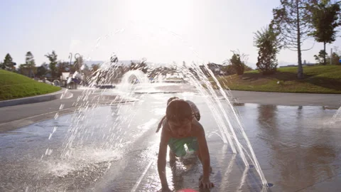 Two children crawl under water arches at splash pad in summer, slow motion Video stock 233943525