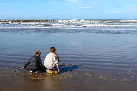 Two children explore shallow beach water with sticks Stock Photos