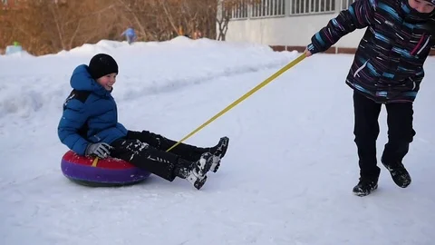 Two children have fun playing on snowtube spinning in a circle. Slowmotion Vidéo 70675168