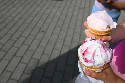 Two children hold scoops of ice cream in waffle cones on a paved outdoor walk Photos