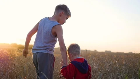 Two children holding hands walking on wheat field. Sunset Видео 79819921
