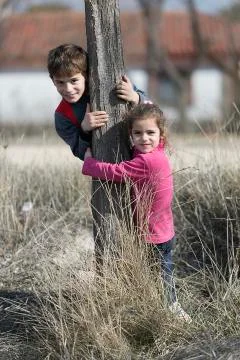 Two children hugging a trunk of a tree smiling. Stock Photos