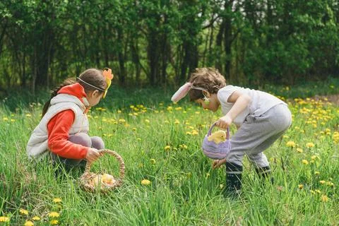 Two children hunt for Easter eggs in a spring garden. Easter tradition Stock Photos