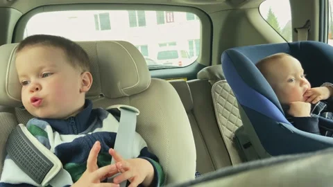 Two children inside driving car fastened car chair kids. 4 year boy baby brother Stock Footage 238727760