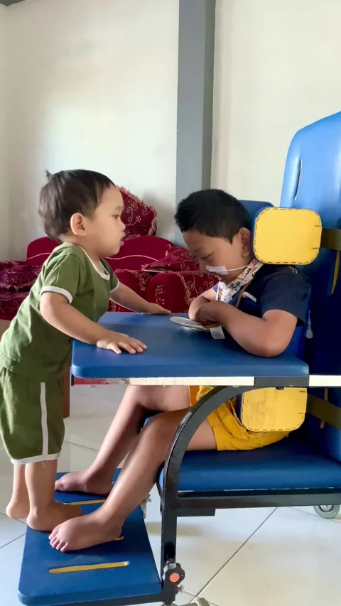 Two children interacting at home with a specialized chair Stock Footage 342090602