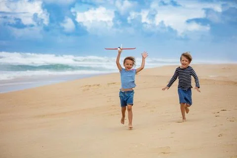 Two children joyfully running playing with a toy planer on beach Stock Photos