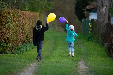 Two children joyfully walking down a lush green path, holding colorful ball.. 스톡 사진