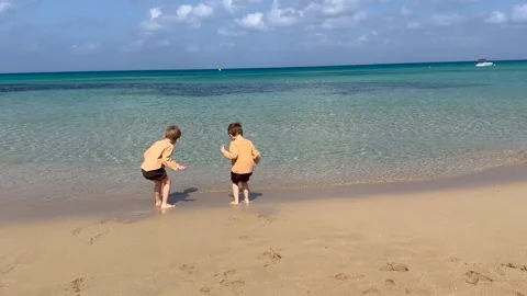 Two children jump into sea waves and play on sandy beach shore in active summer Stock Footage 334321878
