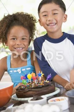 Two children in kitchen with birthday cake smiling Stock Photos