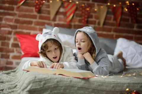 Two children lay on a bed in soft pyjamas. Stock Photos
