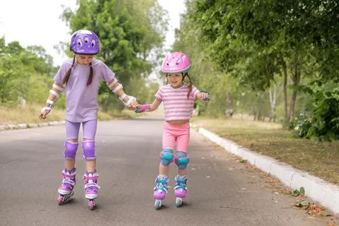 Two children learn to skate roller skating hand in hand. Stock Photos