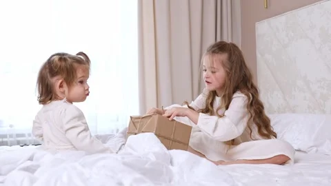 Two children, little sisters sit on bed, open gift boxes wrapped in kraft paper Stock Footage 314063015