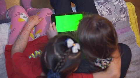Two children look at the tablet with a green background. View from a top. Close- Stock Footage 104780251