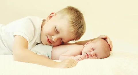 Two children lying on bed, eldest brother and sleeping youngest baby at home Stock Photos