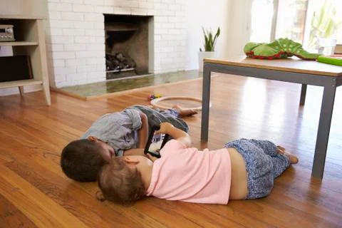 Two Children Lying On Floor Playing With Digital Device Stock Photos