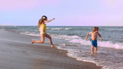 Two Children Make A Game Of Chasing The Waves And Jumping In Them Vídeos de archivo 37042599