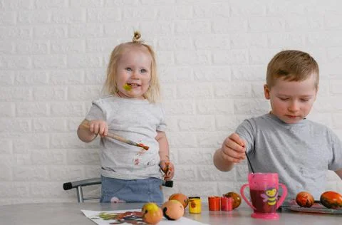 Two children paint eggs in the kitchen on the eve of the Easter holiday Stock Photos
