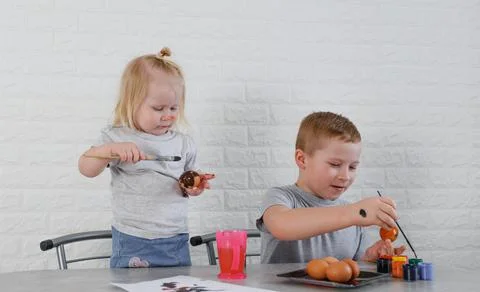 Two children paint eggs in the kitchen on the eve of the Easter holiday Stock Photos
