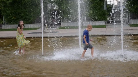 Two children play with the gushing jets of water in the fountain in the summer. Stock Footage 244569020