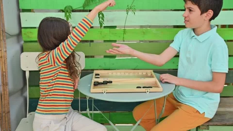 Two children playing backgammon at a small outdoor table Stock Footage 290053485