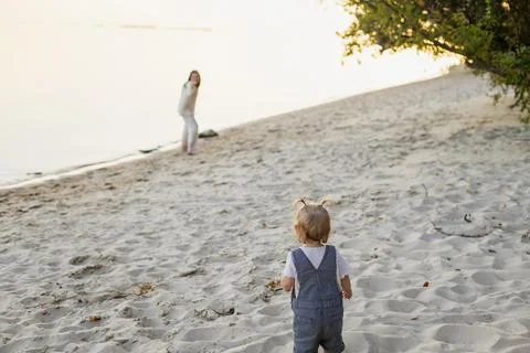 Two children playing on a sandy beach near the water during golden hour Stock Photos