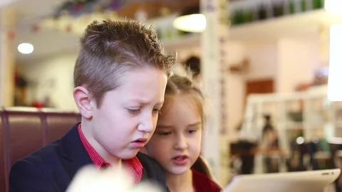 Two children playing in the tablet in a cafe Stock Footage 84177501