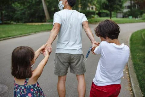 Two children pull on fathers hands as they walk down street together Stock Photos