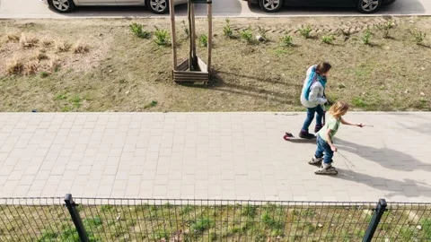 Two children ride on roller skates and a scooter along the footpath Stock Footage 239020924