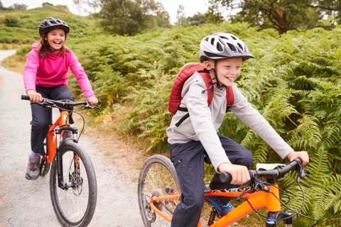 Two children riding mountain bikes on a country path laughing, selective focu Stock Photos
