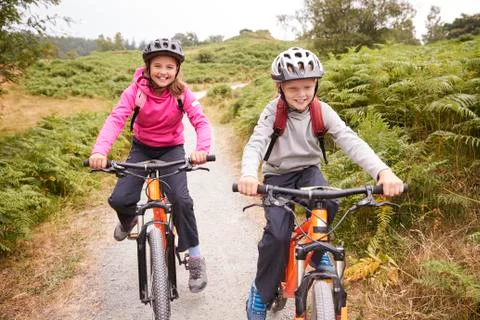 Two children riding mountain bikes on a country path laughing, front view Stock Photos
