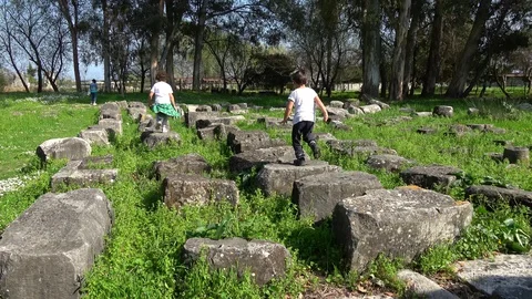 Two children running skip on the ancient columns of the Limyra ruins Stock Footage 127980933