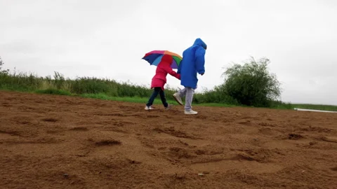 Two children running together on sandy ground under colorful umbrellas, wearing Stock Footage 317553408
