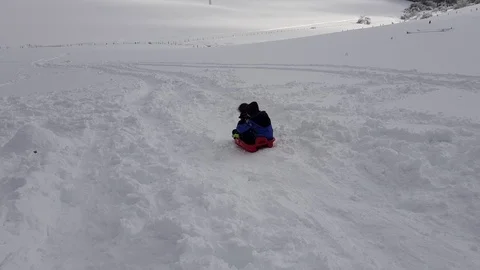 Two children show their excitement by sledding down a hill in winter Stock Footage