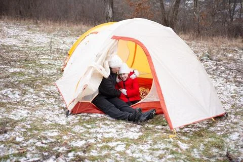 Two children sit closely inside a tent, wrapped in warm clothing, enjoying ea 스톡 사진